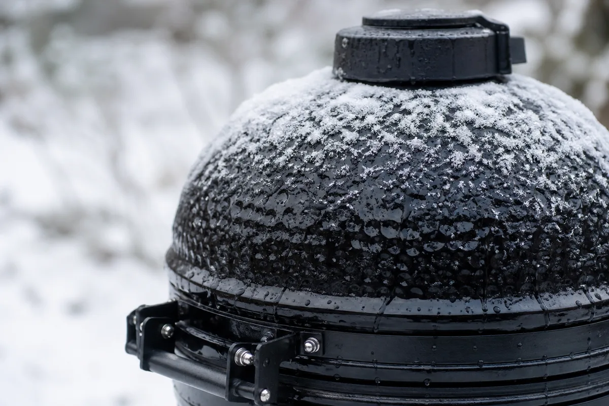 Kamado en céramique posé sur une terrasse enneigée, dôme fermé, fumée légère