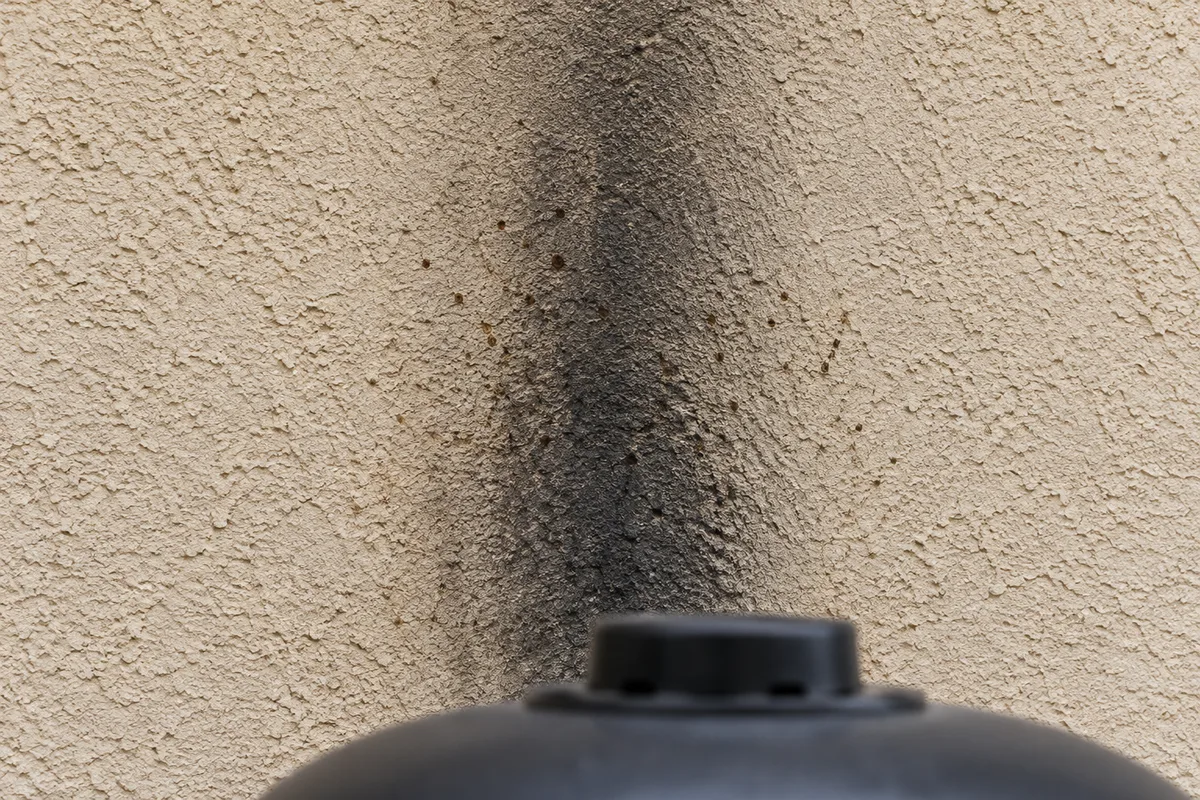 Mur en crépi beige d&rsquo;une terrasse marqué par un voile de suie noire au-dessus d&rsquo;un barbecue céramique